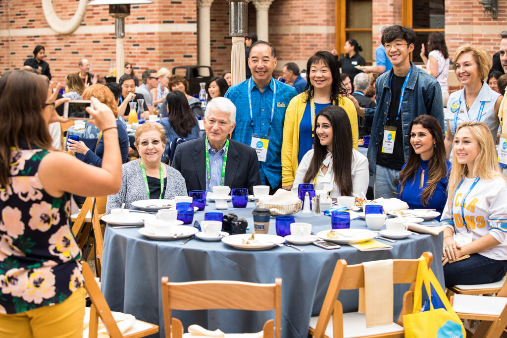 Chancellor Block and Carol Block pose with students, during a meal, during Bruin Family Weekend. 