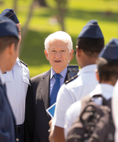 Chancellor Block stands outside (during the daytime) with military personnel wearing hats at the 2022 Memorial Ceremony. 