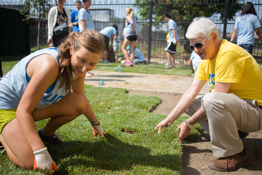 Chancellor Block joins a student volunteer in tamping down new turf at the Nickerson Gardens housing project.
