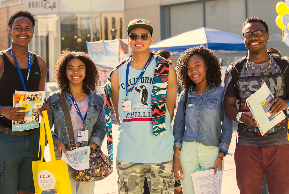 Students posing together in the sun, carrying bags during UCLA Bruin Day. 